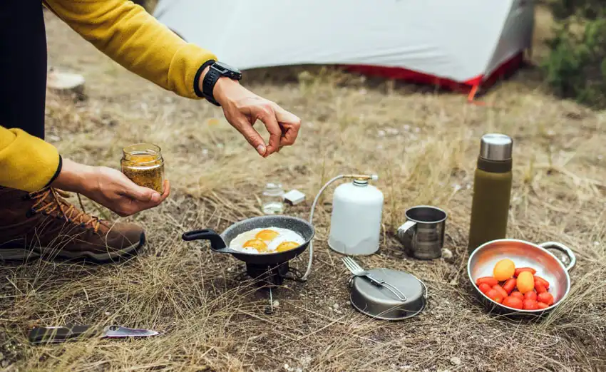 Man cooking eggs using cast iron cookware over a portable camp stove